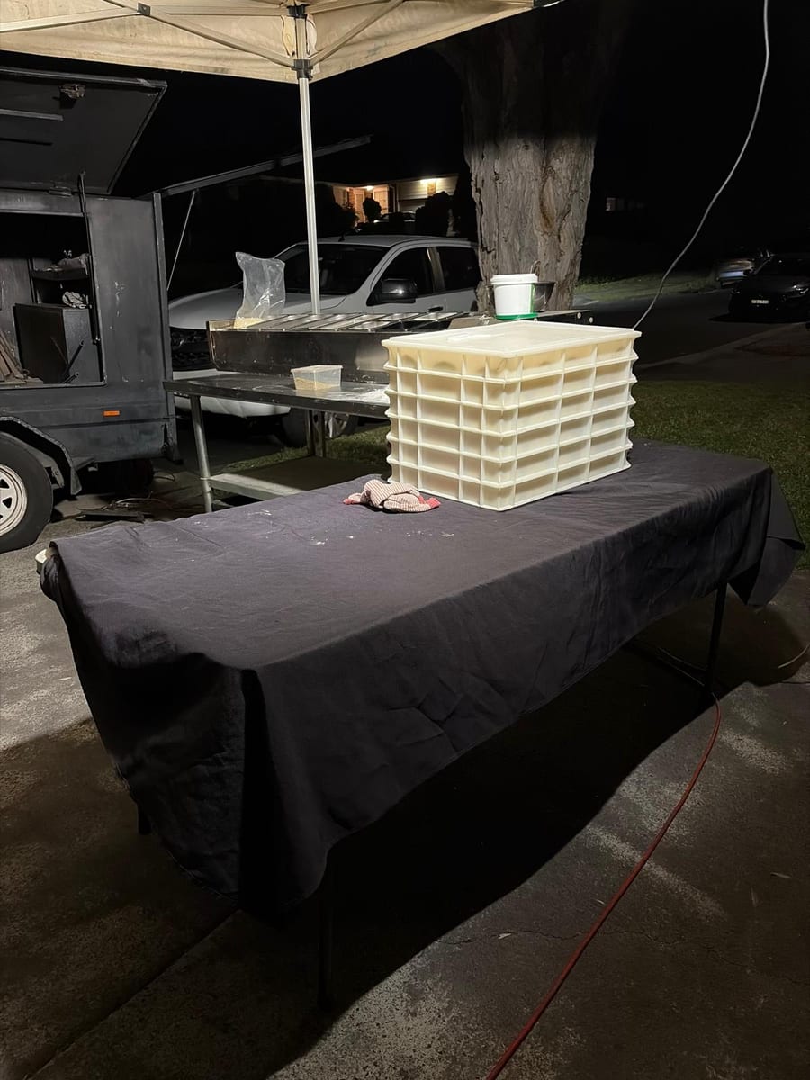 The pizza trailer and prep table set up under a marquee after dark, dough trays stacked ready