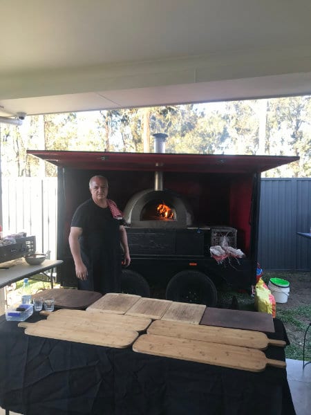 Joe beside the red pizza trailer with the oven lit and serving boards laid out ready