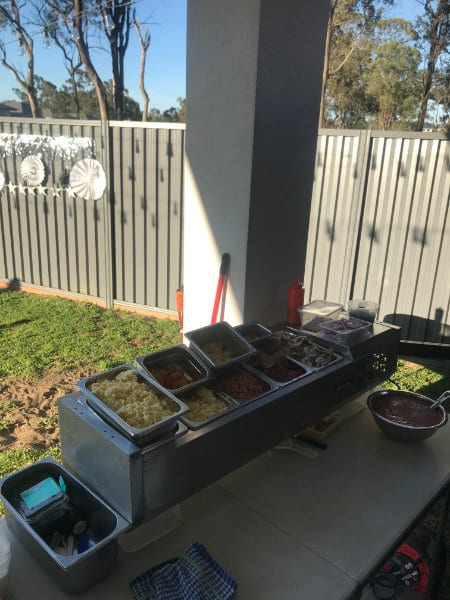 Trays of prepared pizza toppings lined up at the outdoor serving station